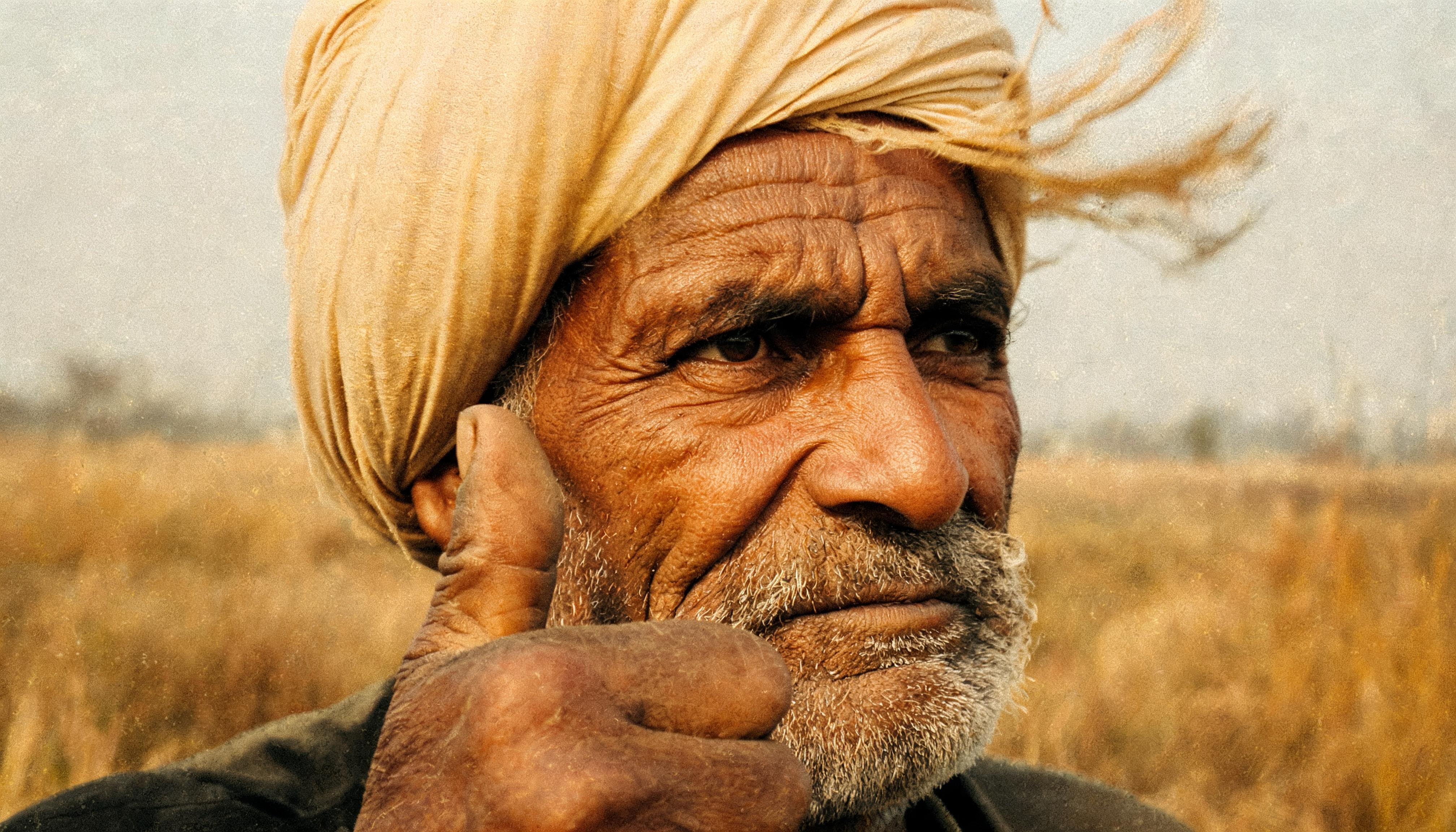 Candid documentary portrait, weathered elderly Punjabi man glancing off frame past his calloused thumb,&hellip;